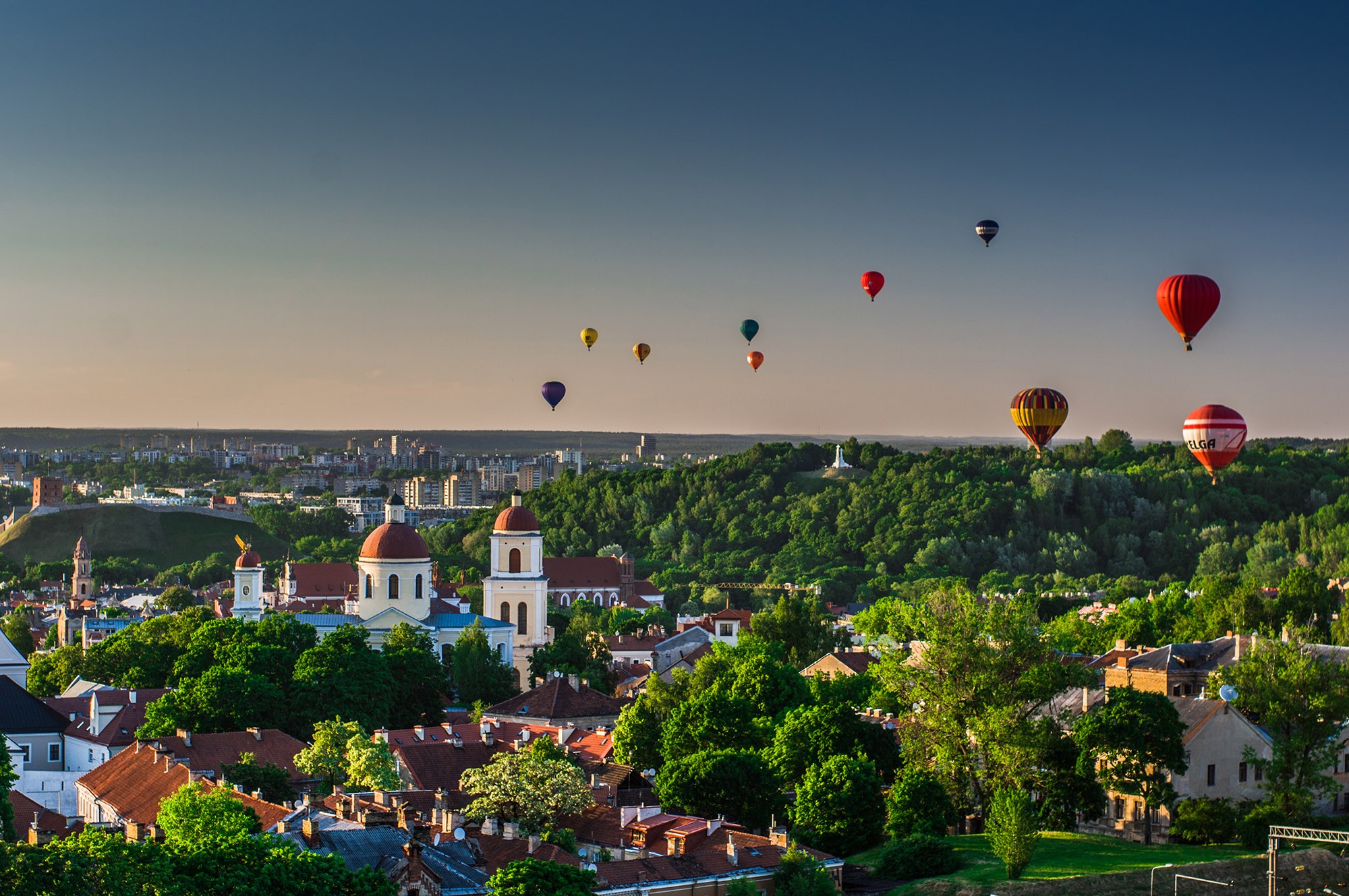 Hot-air balloons above Vilnius at sunset, with the Old Town and Gediminas Hill below